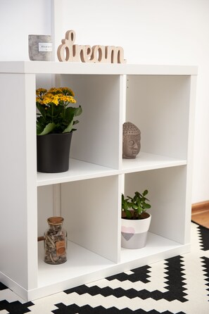 Shelves display a sign, a pot with flowers, a sculpture, a heart-shaped pot, and a jar with small items.