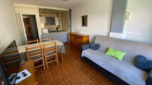 En kompakt opholdsstue med spiseplads, tekøkken og en sofa med puder.