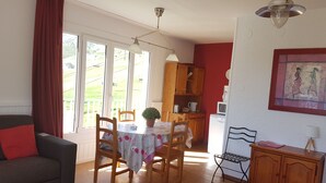 En hyggelig stue med en sofa, et spisebord med stole, et køkken med træskabe og et stort vindue med gardiner.