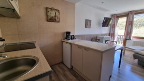A compact kitchen with a sink, a coffee maker, and a small refrigerator. There is a dining area with a table and chairs, and a TV mounted on the wall. - GRIZZLY 106- apt 1 hab -balco- 10 m piste- Pas de la Casa 005794 (Pas de la Casa)