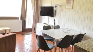 A dining area with a white table, black chairs, a TV on the wall, and a window with curtains. - GRIZZLY 203-apt-1 hab 5 pers-balco-10 m piste-Pas de laCasa-005865 (Pas de la Casa)
