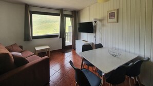 A room with a sofa, a dining table with chairs, a TV, and a window with curtains. - GRIZZLY 203-apt-1 hab 5 pers-balco-10 m piste-Pas de laCasa-005865 (Pas de la Casa)