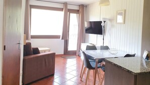A room with a sofa, a dining table with chairs, a TV, and a lamp. - GRIZZLY 203-apt-1 hab 5 pers-balco-10 m piste-Pas de laCasa-005865 (Pas de la Casa)