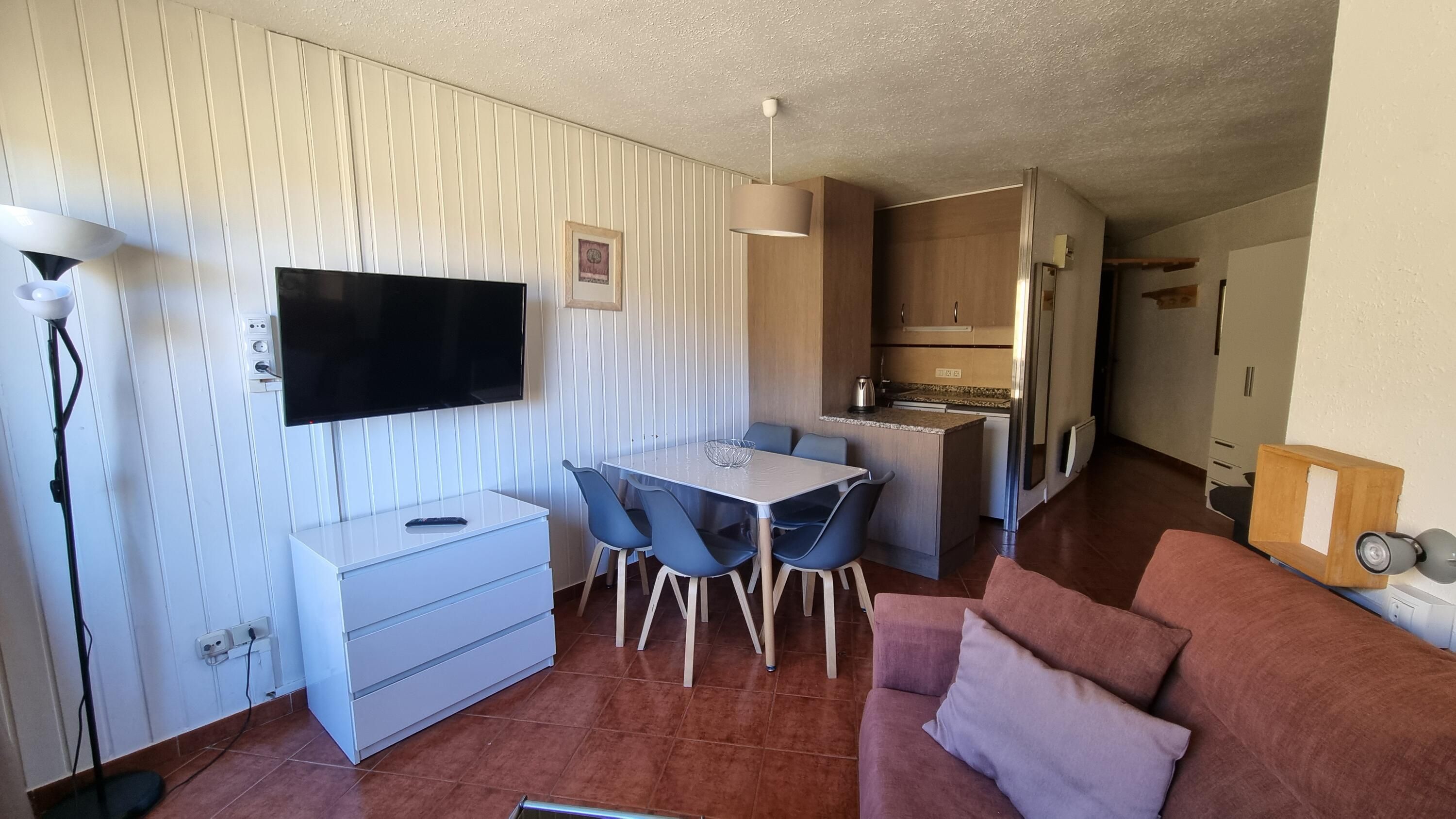 Un espace de vie compact comprenant un coin repas, une kitchenette et un téléviseur fixé au mur.