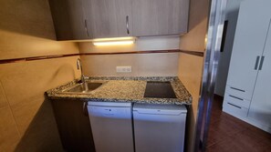 A compact kitchen with a built-in dishwasher, a granite countertop, and a stainless steel sink.