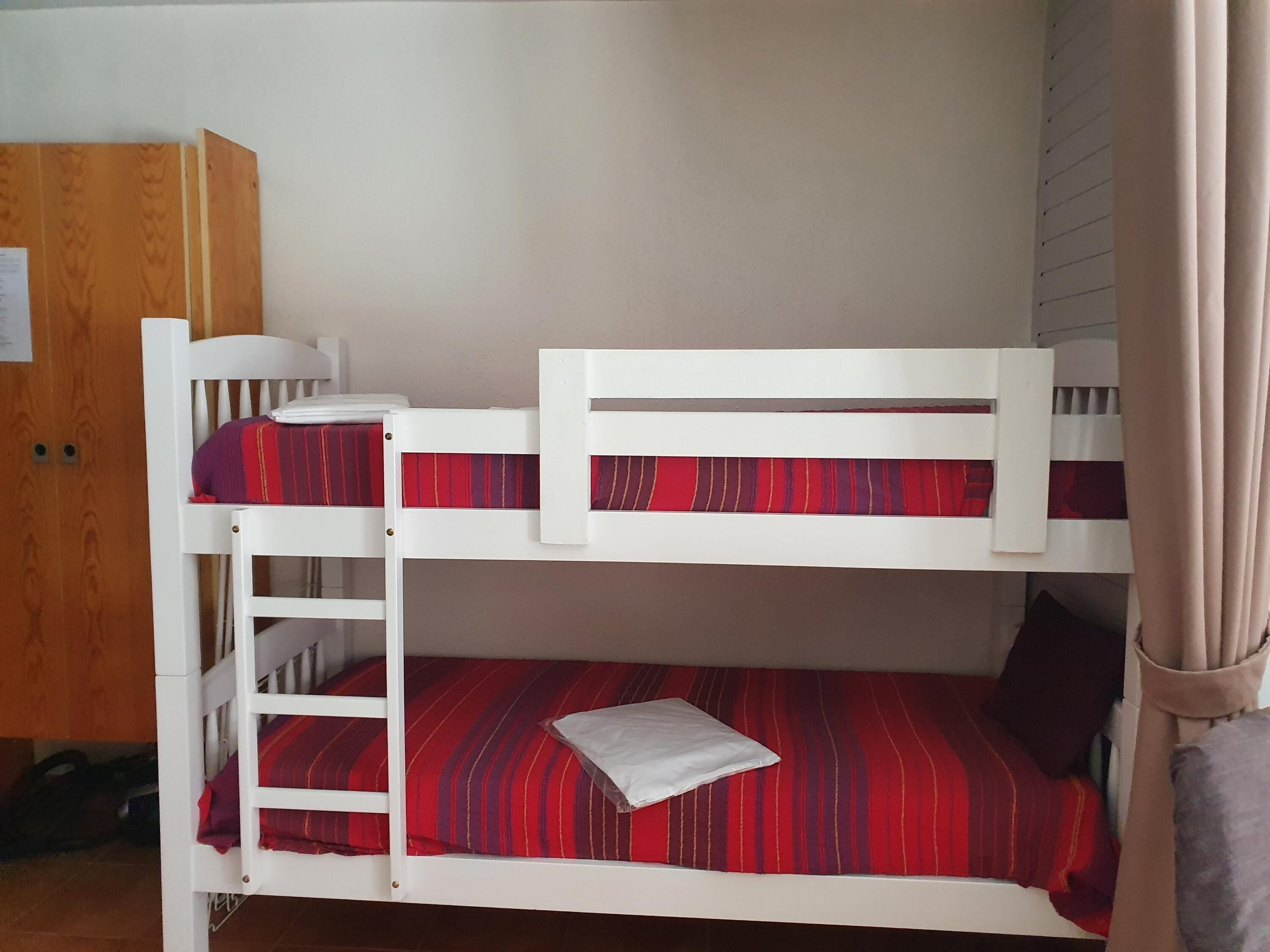 Una cama litera con ropa de cama roja y blanca, un armario de madera y una cortina.