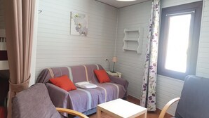 Ett litet, ombonat rum med en soffa, två fåtöljer, ett litet bord, en lampa och ett fönster med gardiner.