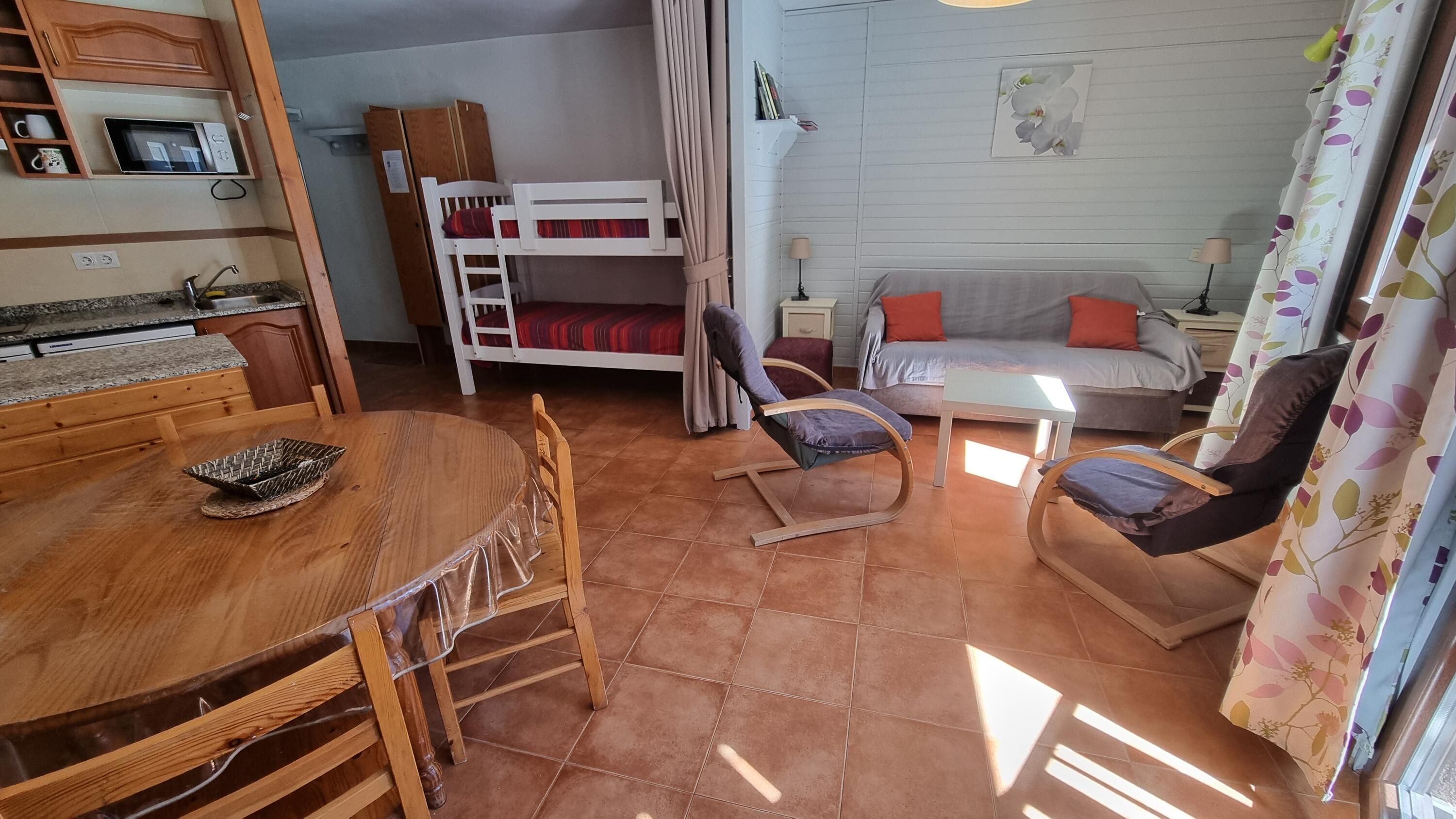 A compact living space with a bunk bed, a dining table with chairs, a sofa, and a small table.