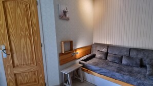 Una stanza con una porta in legno, un tavolino, un divano con cuscini e una mensola a muro con un quadro.