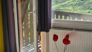 Una stanza con una porta scorrevole in vetro che dà su un balcone, un divano e due tavolini in legno con fiori rossi.