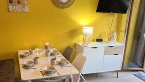 Zona pranzo con tavolo apparecchiato per quattro persone, una candela e una TV a parete.