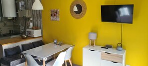 A bright yellow room with a dining table, chairs, a TV, and a kitchen area with appliances.