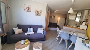 A modern living room with a sofa, coffee table, and dining area. There is a kitchen visible in the background.