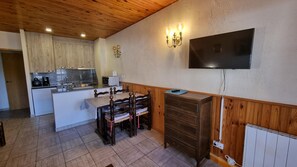 A compact kitchen with a dining area, wooden cabinets, a TV mounted on the wall, and a built-in heater.