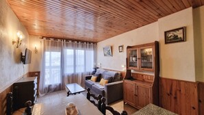 A cozy living room with a wooden ceiling, a grey sofa with cushions, a wooden cabinet, and a television mounted on the wall. - 505 SKY -Apt 1 hab- 4 pers-Pas de la Casa-10 m pistes -005632 (PAS DE LA CASA)