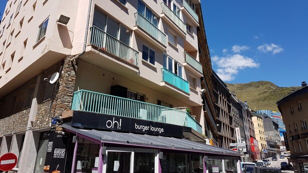 A multi-story building with balconies, a restaurant named "oh! burger lounge" on the ground floor, and a view of a hilly landscape in the background. - 505 SKY -Apt 1 hab- 4 pers-Pas de la Casa-10 m pistes -005632 (PAS DE LA CASA)