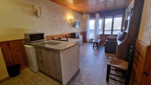 A kitchen with a microwave, a sink, and a wooden cabinet. There is a dining area with a table and chairs.