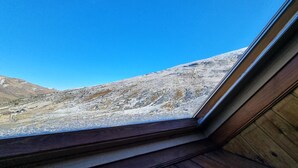 Blick aus dem Fenster auf eine gebirgige Landschaft bei blauem Himmel.