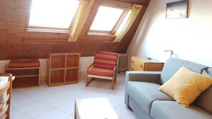 Ein gemütliches Dachzimmer mit Holzbalken, einem Sofa, einem Streifenstuhl und einem kleinen Tisch.