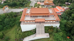 Eine Luftaufnahme eines traditionellen Gebäudes mit einem markanten Mittelbau, einem weitläufigen Innenhof und einer üppigen, grünen Landschaft rundherum.