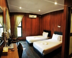 Quarto de hotel com duas camas, painéis de madeira, uma escrivaninha com bandeja, um espelho e um aparelho de ar condicionado.