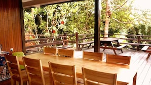 Eine Holzterrasse mit einem runden Tisch und Stühlen, umgeben von einem Holzzaun und Bäumen.