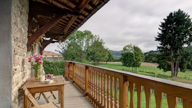 Een houten balkon met een tafel en stoelen, met uitzicht op een groen landschap met bomen en een heuvel in de verte.