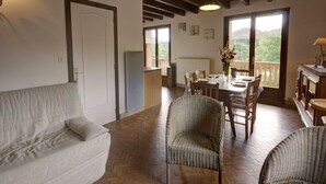 Een gezellige woonkamer met een bank, rieten stoelen, een eettafel gedekt voor twee personen, en een balkon met uitzicht.