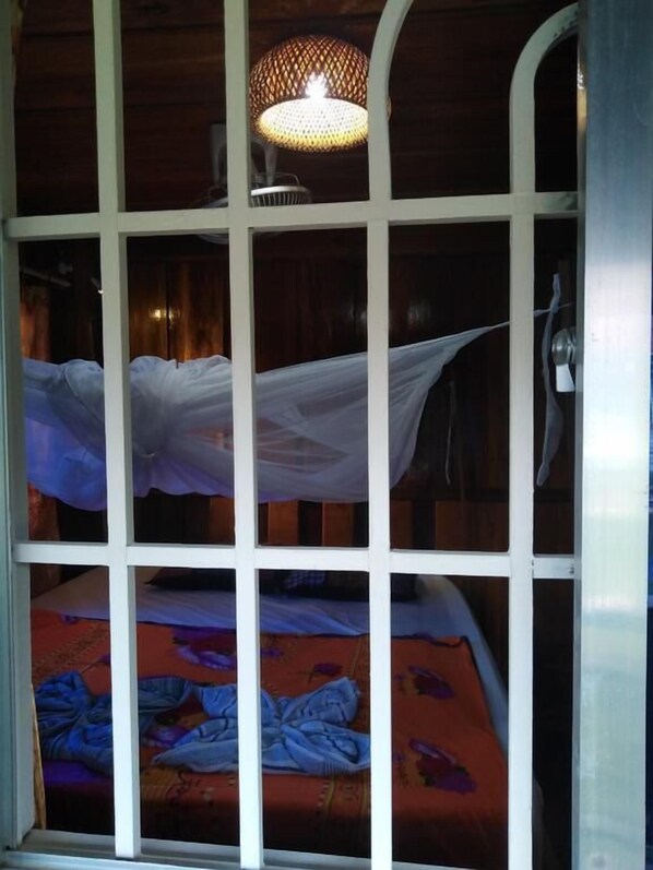 Una habitación con una cama cubierta por un dosel blanco, una lámpara colgante y una ventana con vista al exterior.