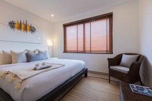 A bedroom with a large bed, a chair, a window with blinds, and a wall art piece.