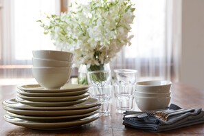 A dining table with stacked plates, glasses, and a folded napkin.