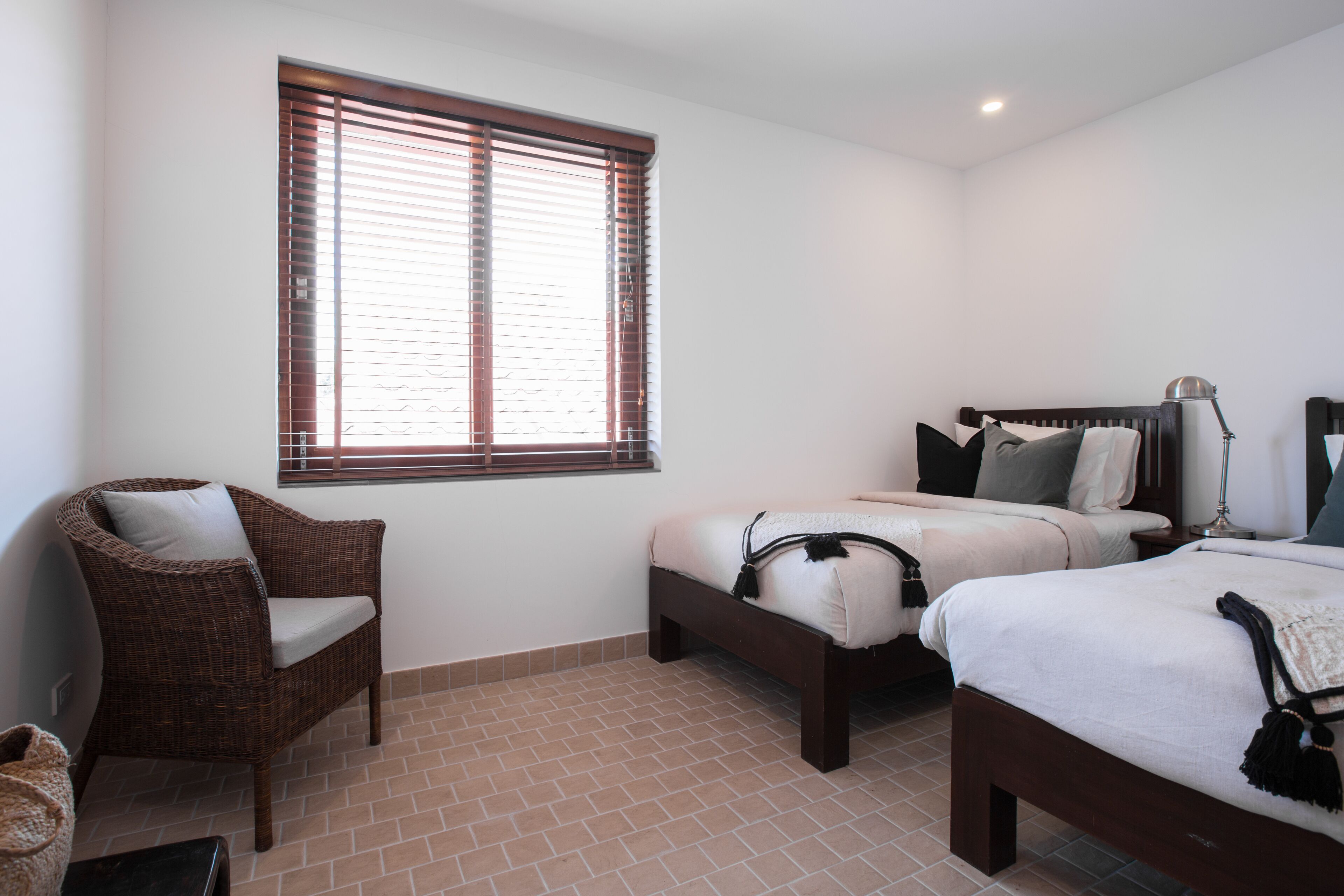Un dormitorio con dos camas, una silla de mimbre y una ventana con persianas.