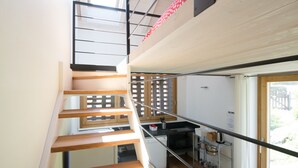 Una escala moderna amb graons de fusta i baranes metàl·liques que condueix a un segon pis, on es veu una zona de cuina.