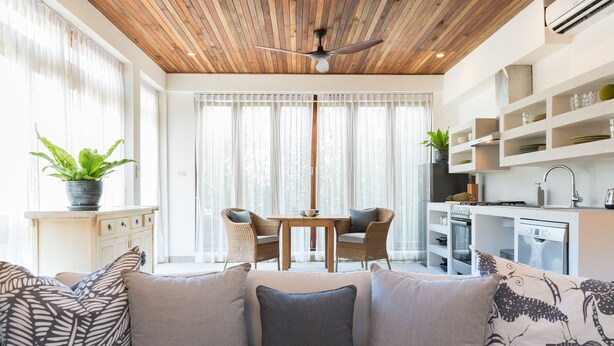 A modern kitchen with white cabinetry, a dining area with wicker chairs, and a ceiling fan. - Papaya Studio (Koh Samui)