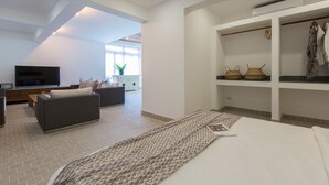 A modern living room with a sofa, TV, and a dining area. There is a large bed with a patterned bedspread. - Papaya Studio (Koh Samui)