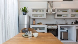 A modern kitchen with white cabinetry, a wooden dining table, and a built-in oven. - Papaya Studio (Koh Samui)