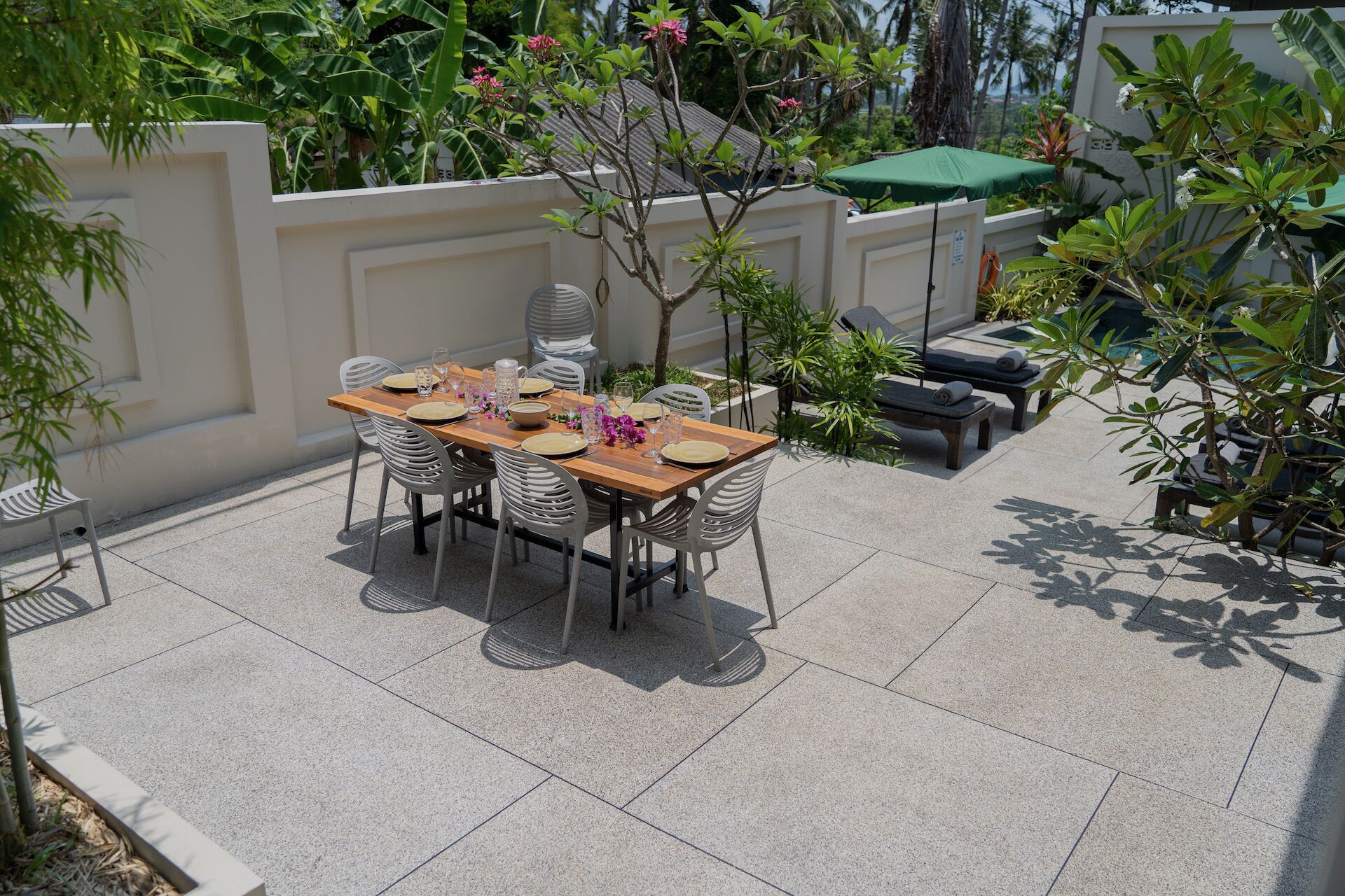 An outdoor patio with a wooden table set for four, surrounded by white chairs.