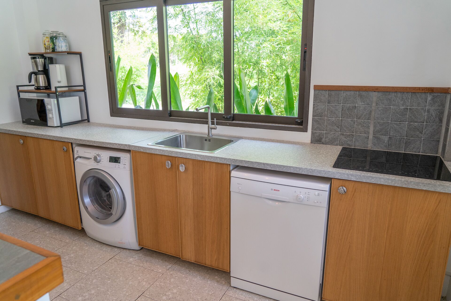 Una cocina con lavadora, lavavajillas y ventana con vistas a zonas verdes.