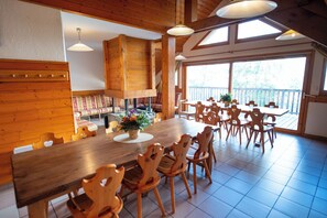 A wooden dining area with a large table and chairs, a staircase, and a view of the outdoors. - Oz/Alpe d'Huez 200m to slopes, up to 25pers, Jacuzzi, 9 en-suite bedrooms (Oz-en-Oisans)