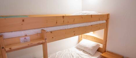 A bunk bed with a green shelf, a bedside table, and a nightstand in a corner room with white walls and wooden beams.