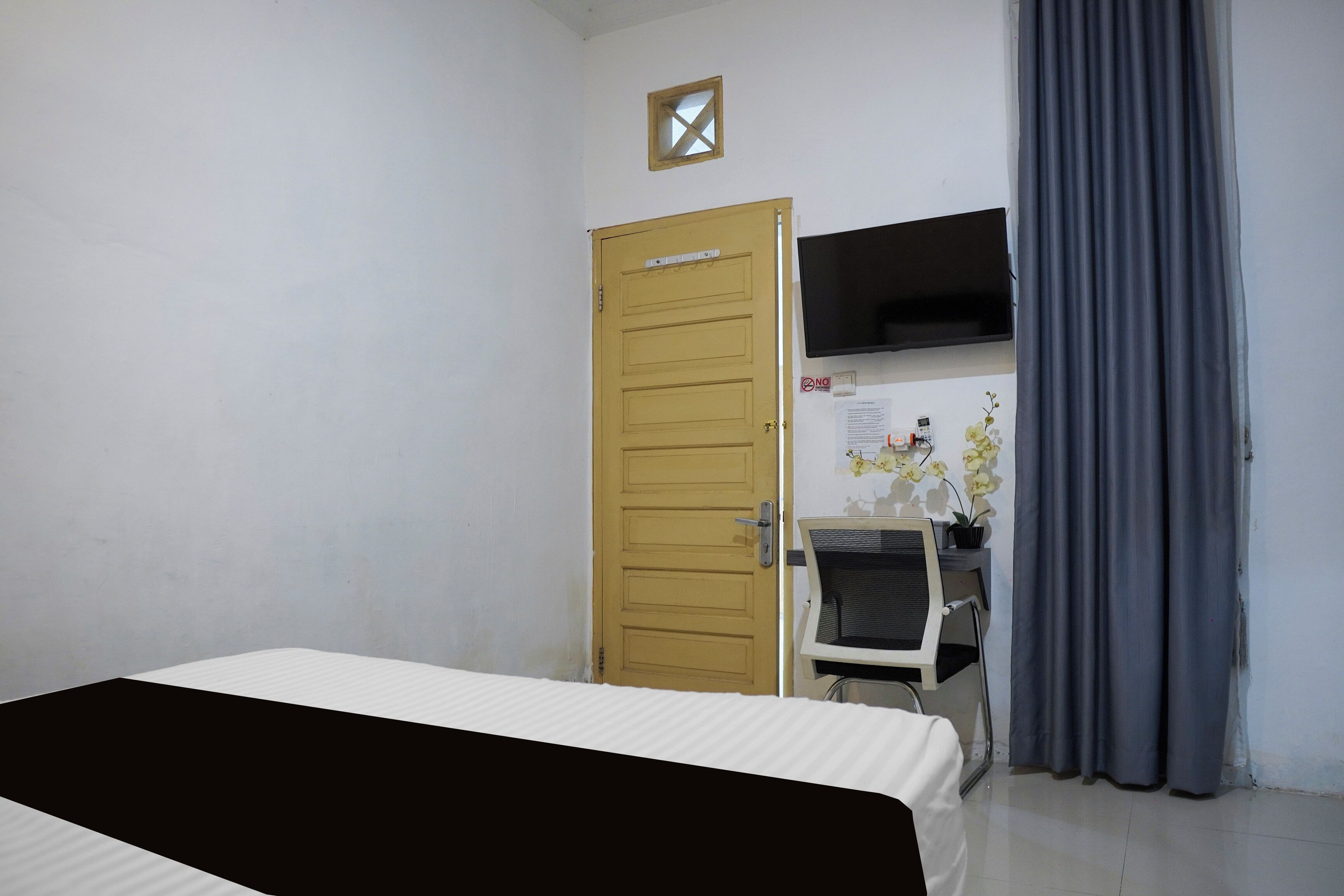 A room with a bed, a desk, a chair, a television, and a door.