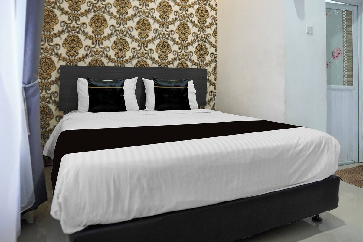 A bed with a black frame and white bedding, a patterned wallpaper, and a door with a floral design.