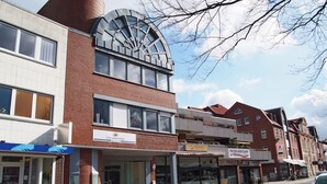 A multi-story building with a modern architectural design, featuring a prominent curved glass facade and a cylindrical structure on the left. - FeWo Borkum in Papenburg (Papenburg)