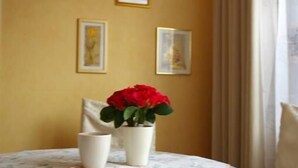 A room with a round table covered by a floral tablecloth, a vase with red flowers, and framed pictures on the wall. - FeWo Borkum in Papenburg (Papenburg)