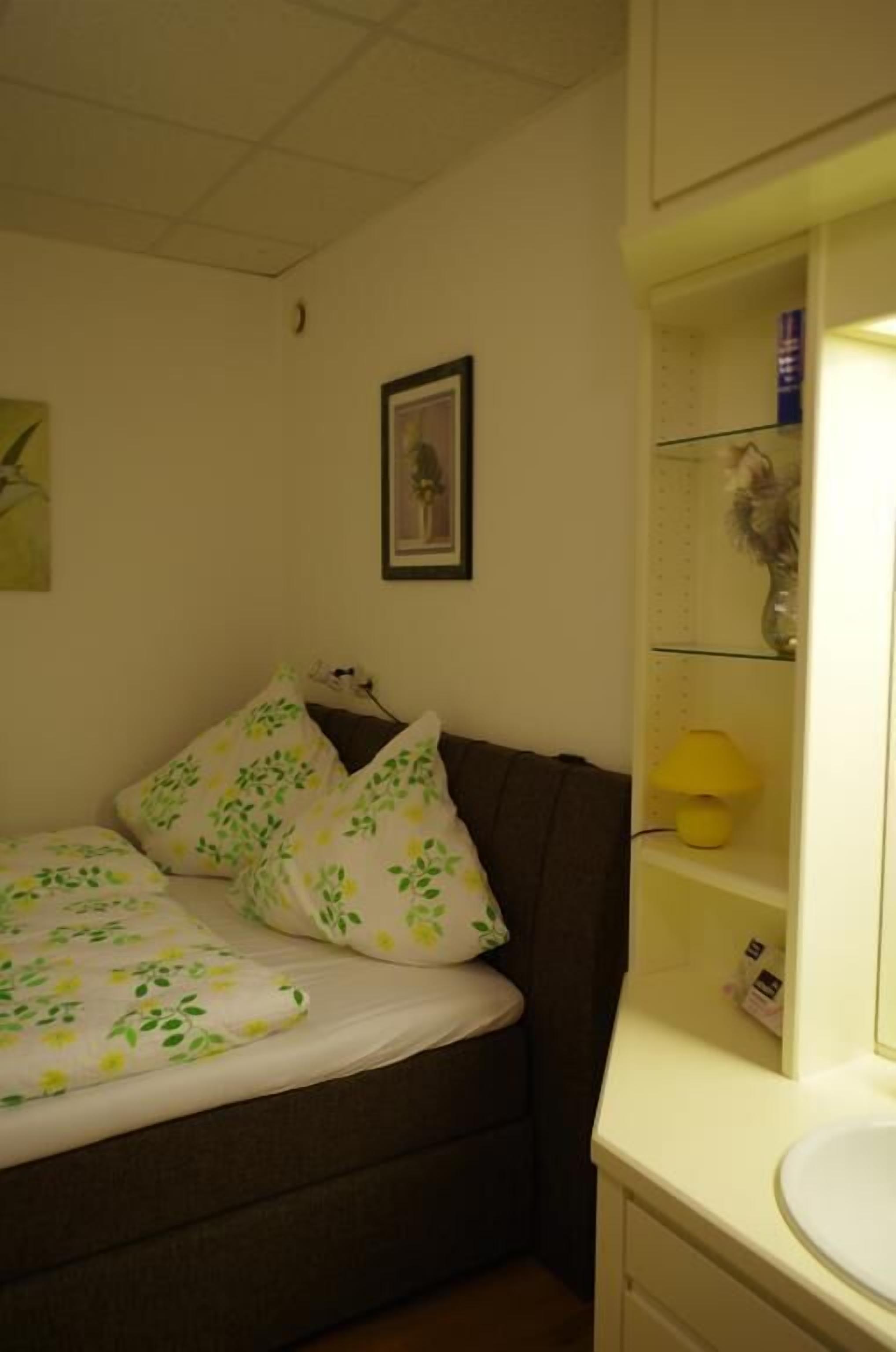 Une chambre à coucher comprenant un lit, une table de chevet, un miroir et une étagère avec une lampe et des objets décoratifs.