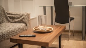 Uma sala de estar moderna com uma mesa de centro de madeira, um vaso de vidro e um controle remoto.