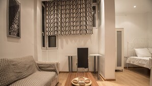 Quarto de hotel com sofá, mesa de jantar com cadeiras, cama e painel decorativo fixado na parede.
