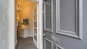 Een gang met een grijze deur, een witte dressoir en een spiegel.