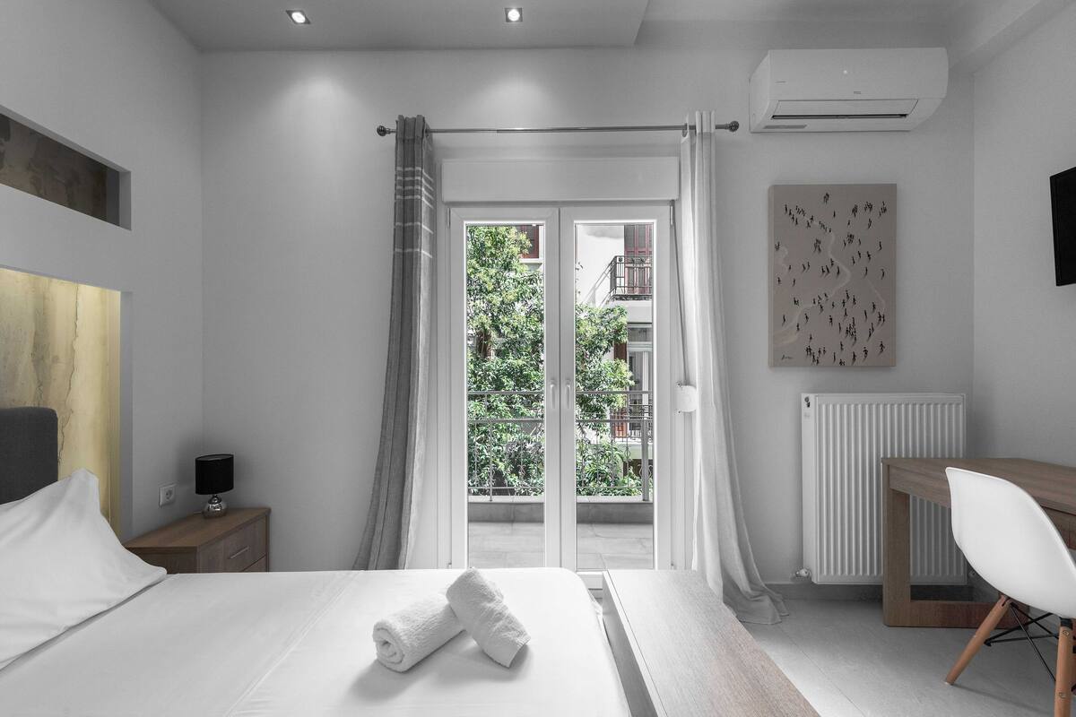 A modern bedroom with a bed, a desk, and a view of greenery outside.