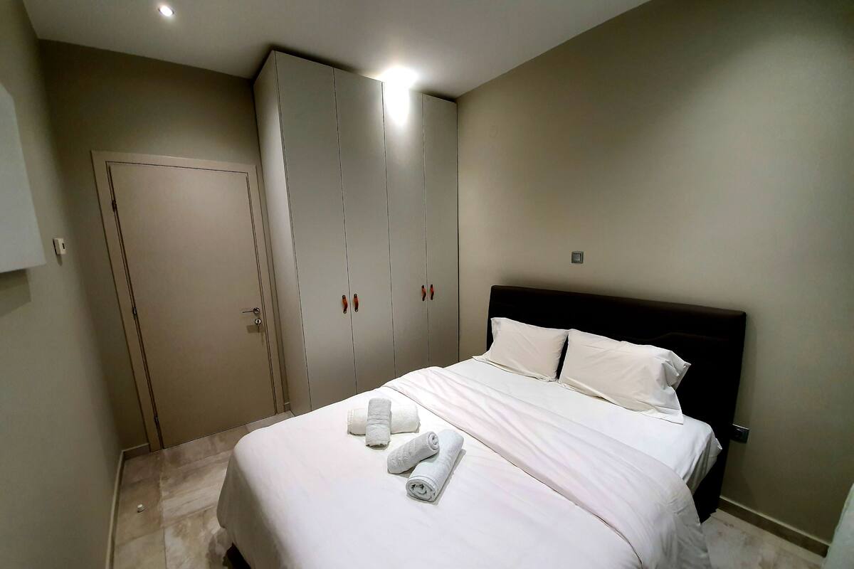 A bedroom with a bed, white linens, a dark headboard, and a wardrobe with sliding doors.